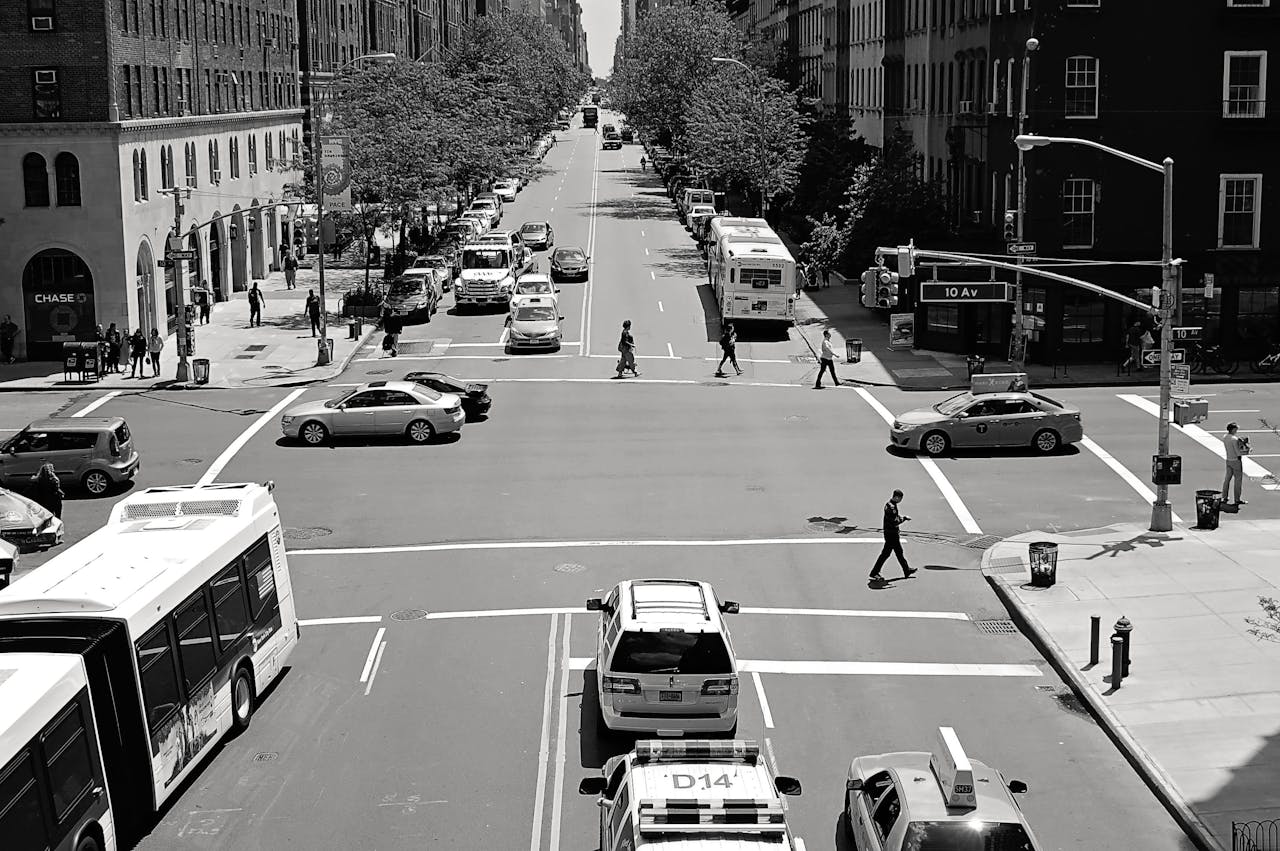 Black and white view of a busy street intersection in New York City with cars, buses, and pedestrians.